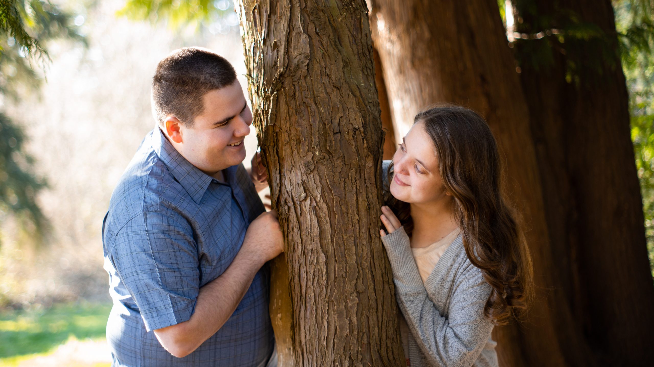 High quality photo of cute couple looking at each other around a tree trunk